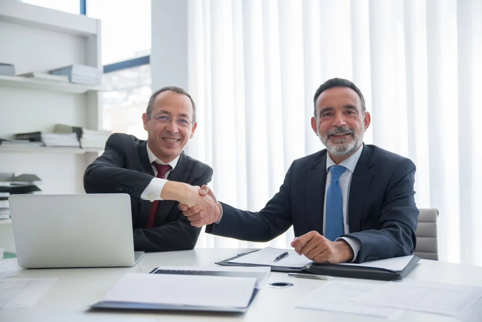 Two businessmen shaking hands across a desk
