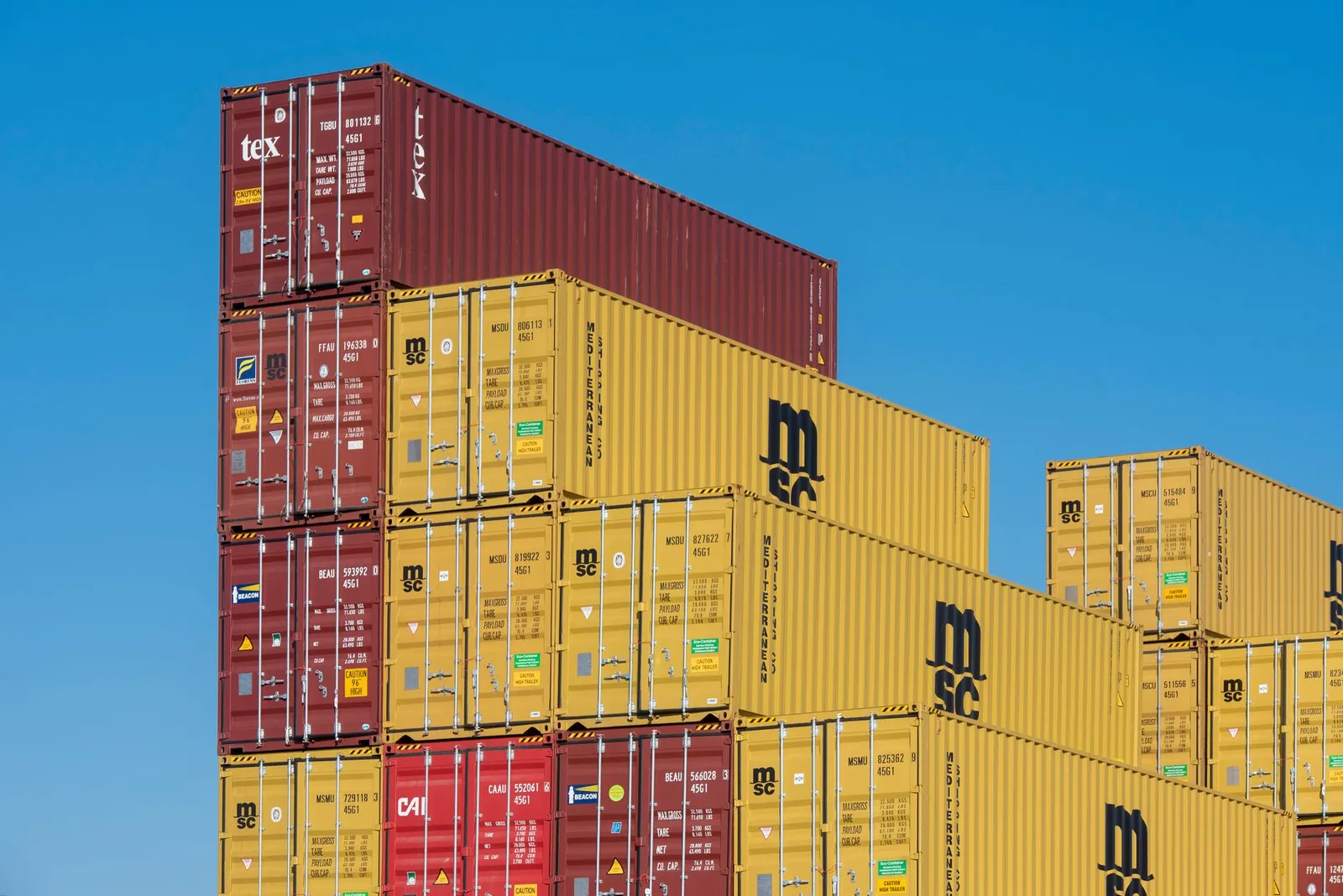 Yellow and red 20FT and 40FT standard dry general-purpose shipping containers stacked against a blue sky