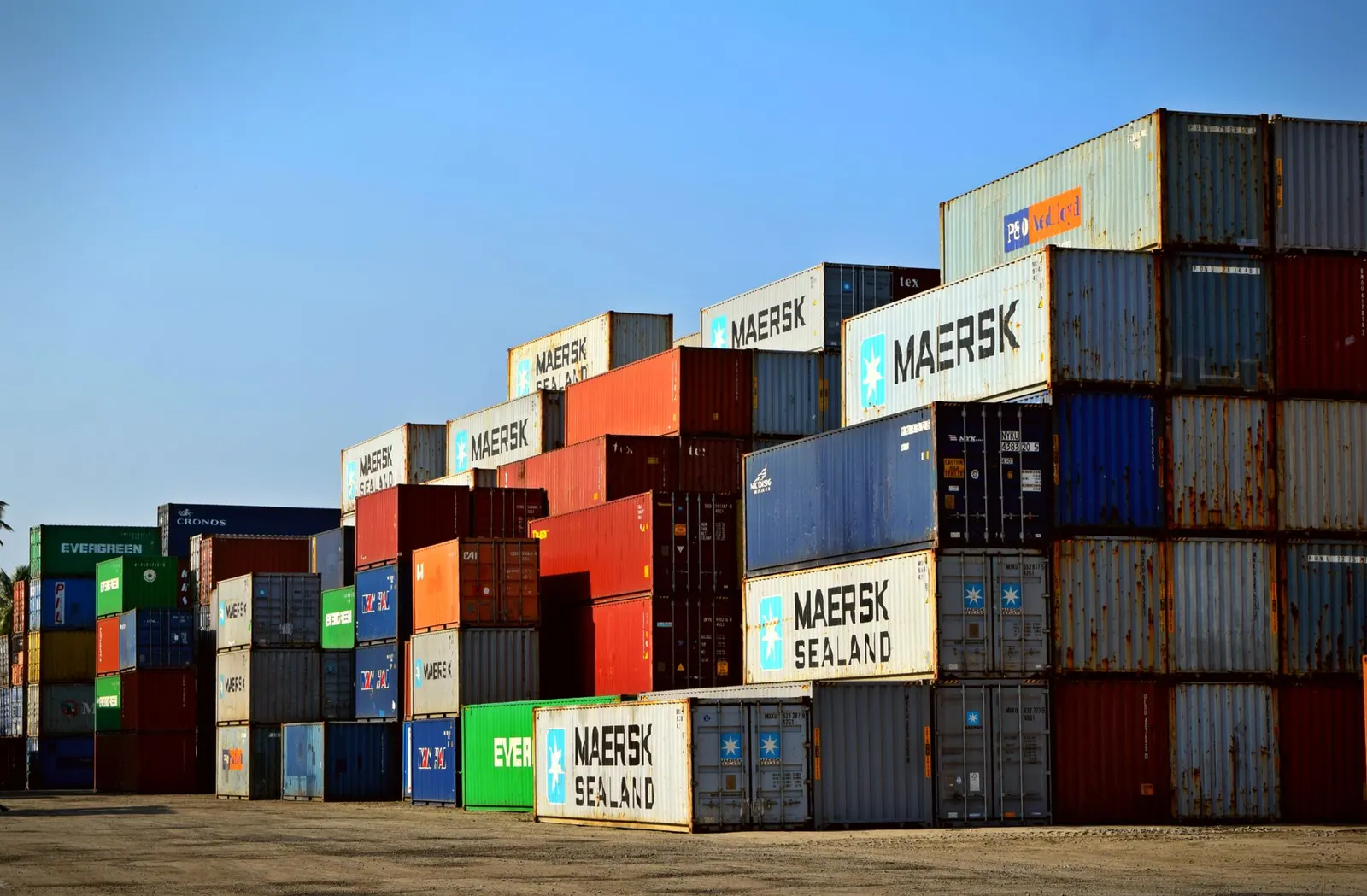 Stacks of 20FT and 40FT shipping containers in a container yard under blue sky